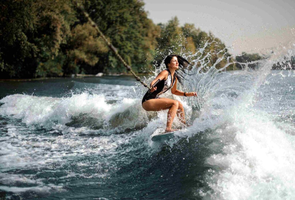 beautiful girl with black hair rides a wakeboard on the waves holding the rope with one hand on the background of beautiful water and nature