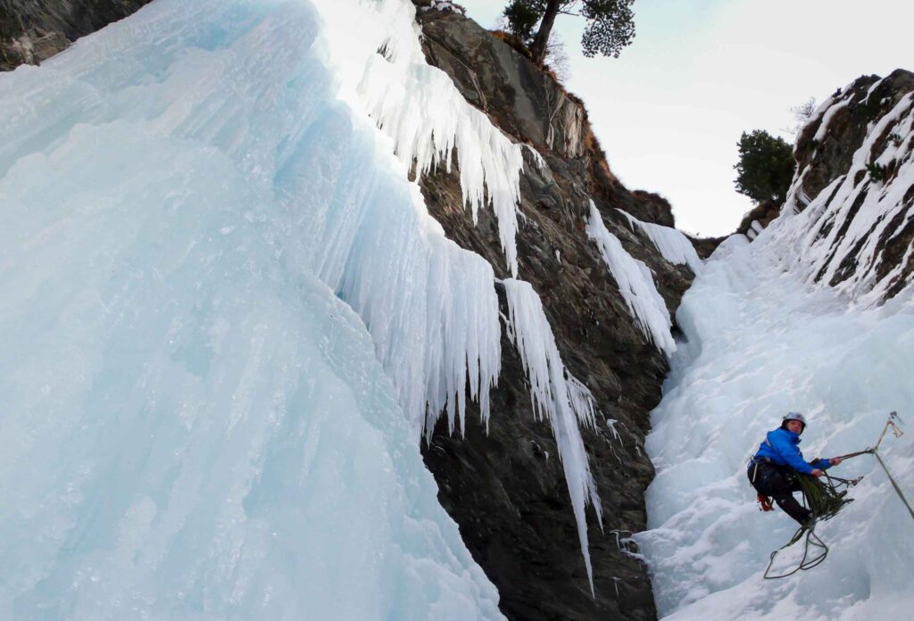 Ice climber in blue outfit crawls on a rock covered with ice with the help of mountaineering equipment