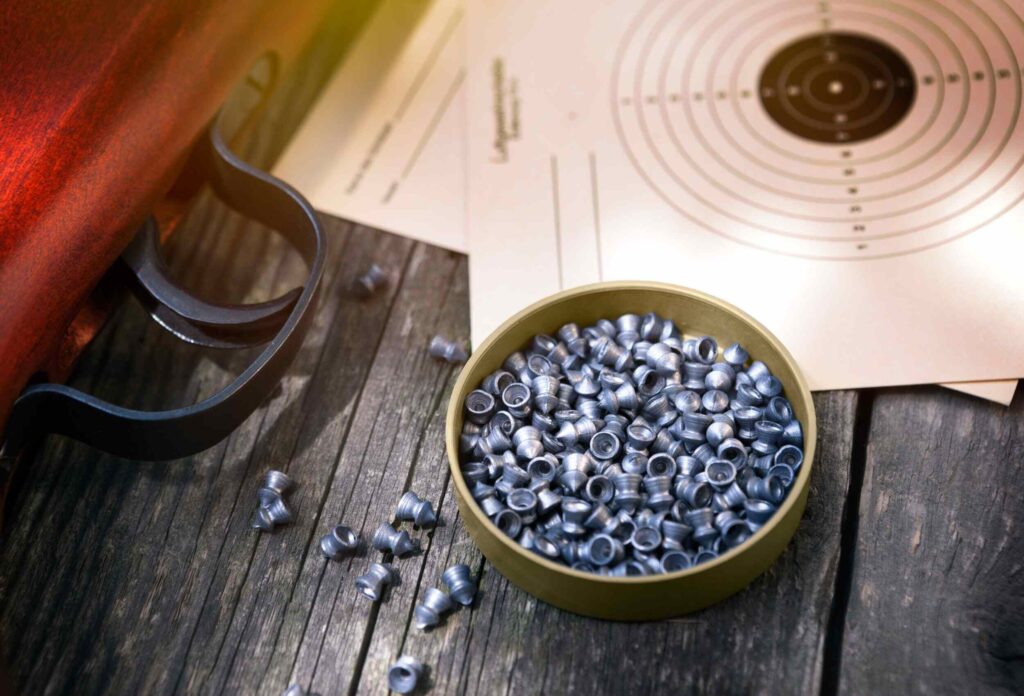 Close-up photo, air rifle bullets are lying on a wooden surface, you can see the trigger of the rifle and targets for shooting