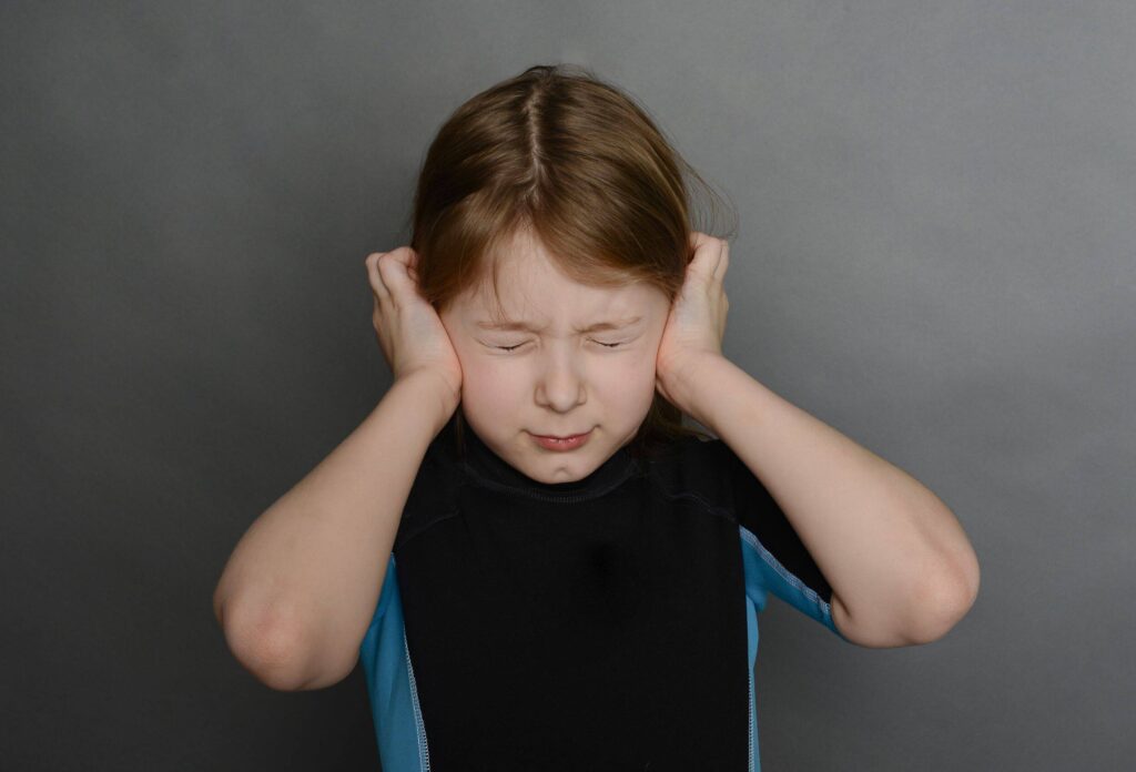 A little girl in a black and blue wetsuit is holding her ears and wrinkling her face because she got a barotrauma to her ear