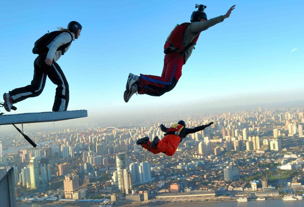 photo of 3 basejumpers jumping from a great height one after another in the background of a big city