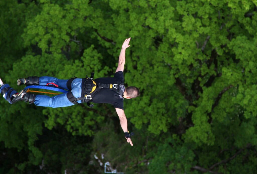 A man bungee jumps above lush green trees