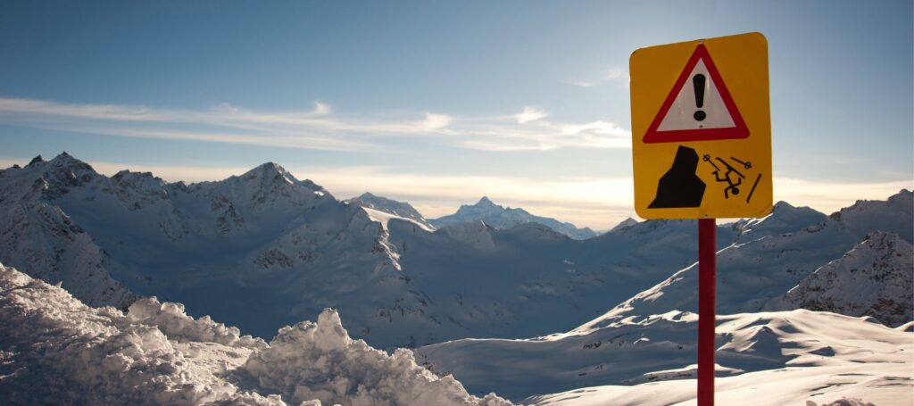 a danger sign on the background of mountains in snow with a skier falling off a cliff on it