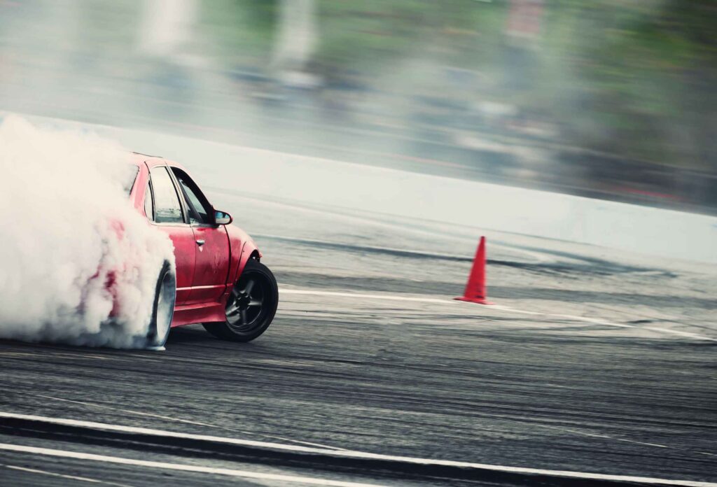 professional racer passes the track in a drifting race on a red car creating smoke from under the wheels