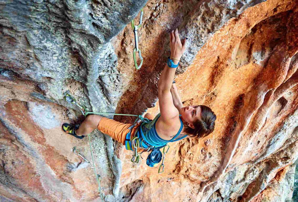 girl rock climber in a blue T-shirt and orange shorts climbing a difficult route on a steep cliff