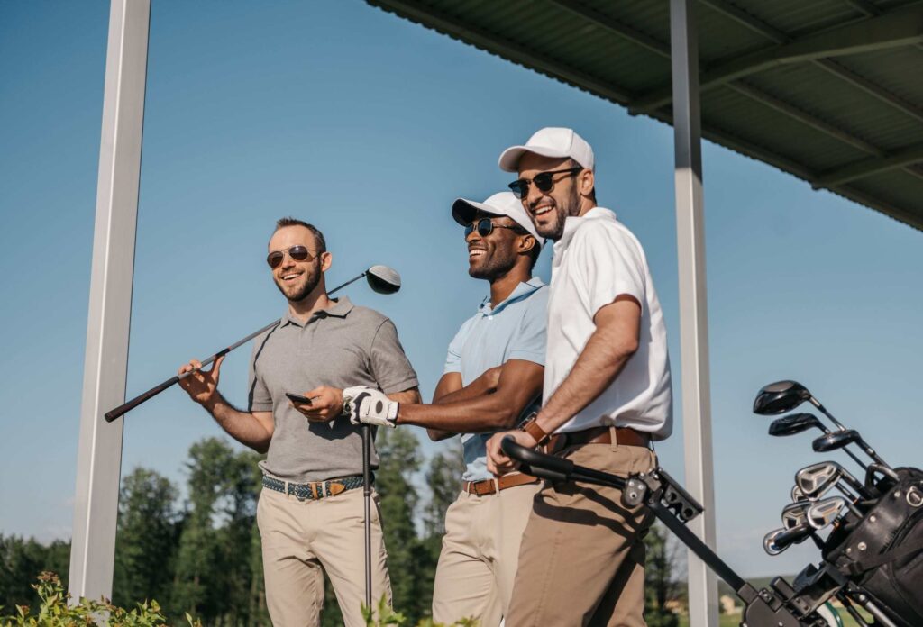 3 handsome men with golf clubs in hand smile while chatting at the golf club