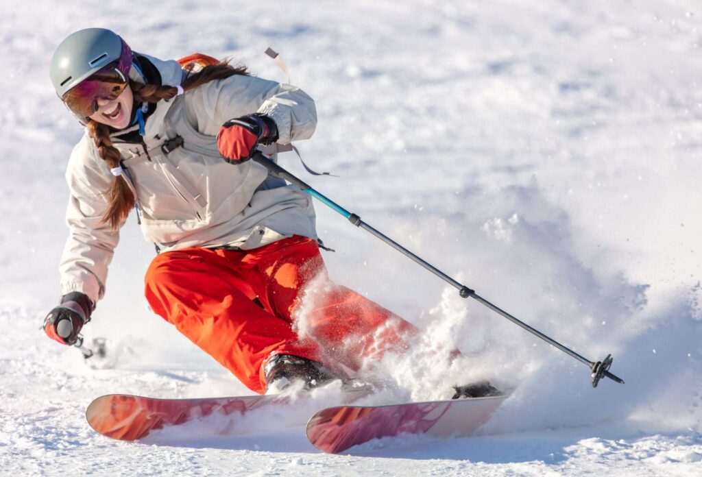 a girl in orange pants and pigtails is skiing and smiling broadly with happiness