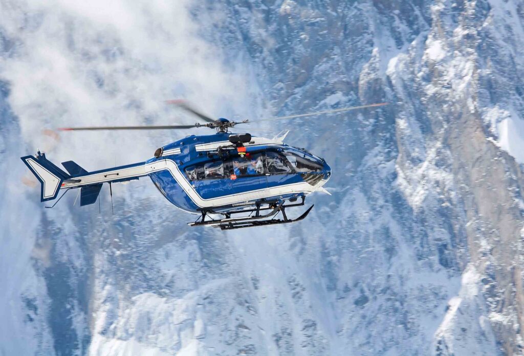 A helicopter to evacuate injured skiers flies against a backdrop of snowy mountains