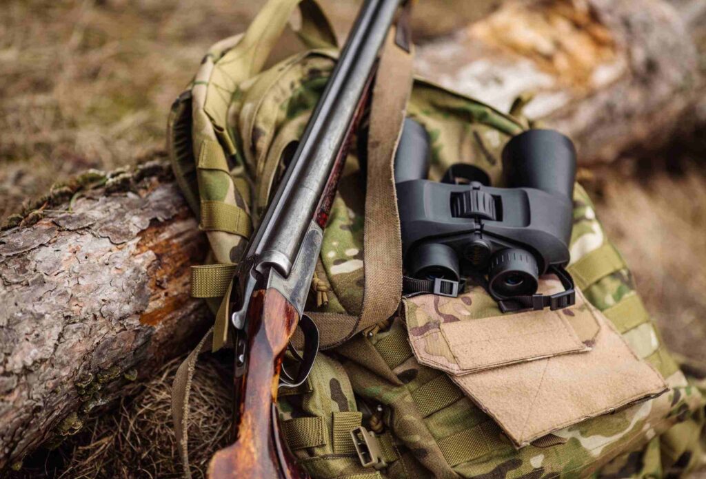 hunting rifle and binoculars on a camouflage-colored backpack on a log