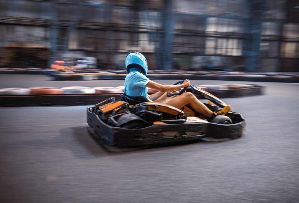 A man wearing a blue helmet and blue T-shirt competes in an amateur karting race on an orange go-kart