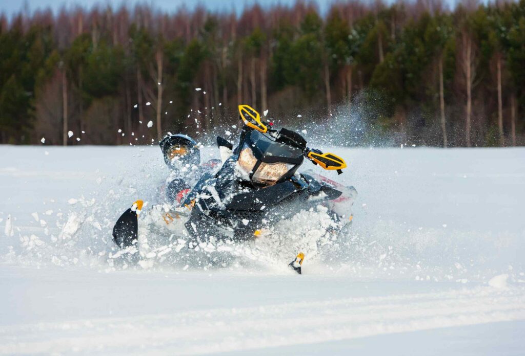 a man dynamically falls from a black-and-yellow snowmobile in deep snow against the background of trees