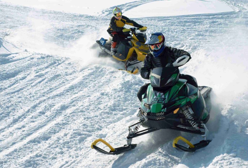 two people riding green and yellow snowmobiles in deep snow