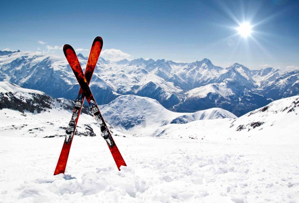 Red and black skis stuck crosswise in the snow against a backdrop of beautiful snowy mountains