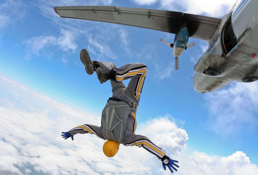 a man in a gray suit and yellow helmet makes an extreme skydive jump jumping headfirst against the background of an airplane