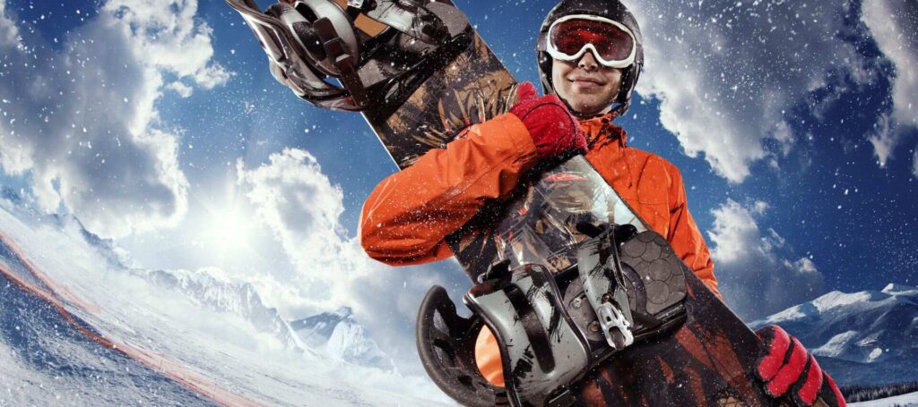 snowboarder in an orange jacket and red gloves holding a beautiful snowboard against the blue sky