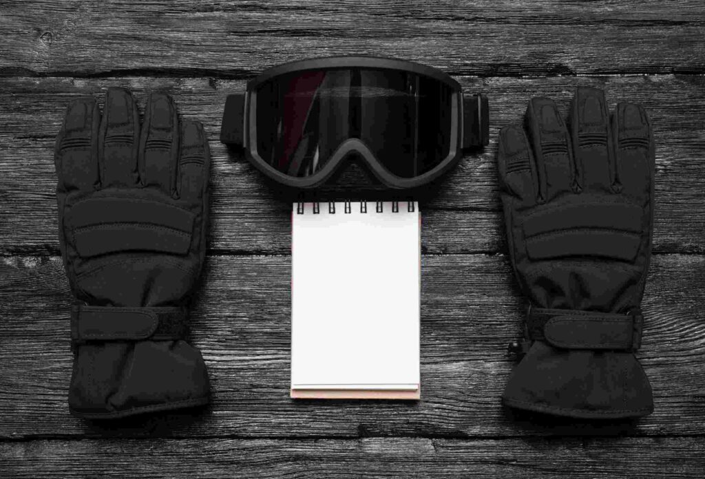 on the wooden surface there are ski gloves and goggles, and in the middle there is a pen and noteb