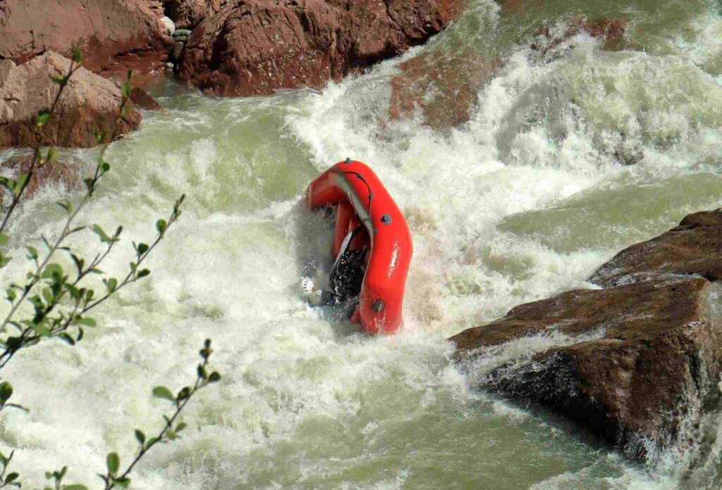 red raft overturned while going through extreme rapids between rocks on rushing water