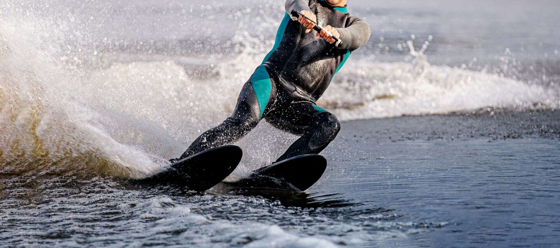 man water-skiing in a black wetsuit with blue inserts creating a splash of water