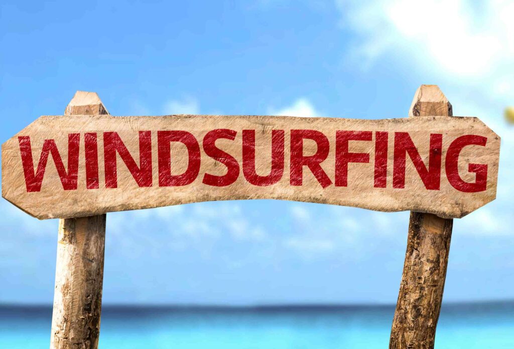 wooden sign with windsurfing inscription in close-up on the background of the beach and water