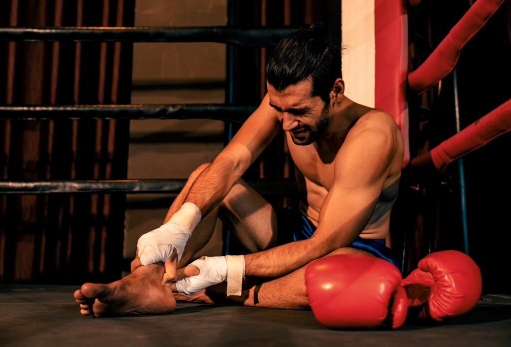 The fighter sits in the corner of the ring holding onto his injured leg