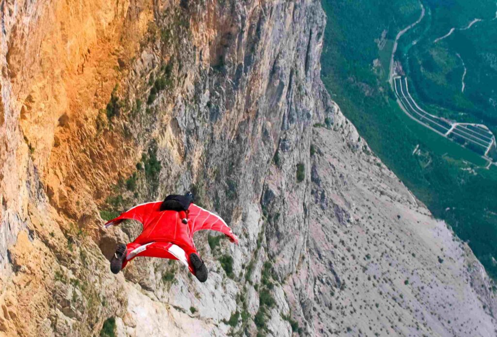 a man in a red wingsuit flies dangerously close to the cliff