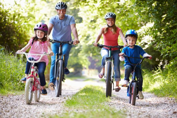 a family with 2 small children riding bicycles on a dirt road