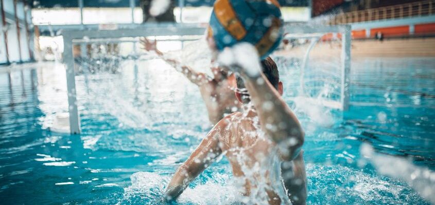 a man throws the ball into the goal at water polo