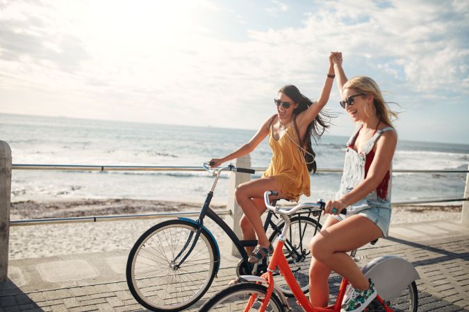 beautiful girls riding along the embankment on bicycles and holding hands